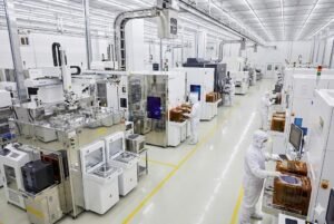 Interior of a high-tech semiconductor manufacturing factory with workers wearing protective suits operating machines.