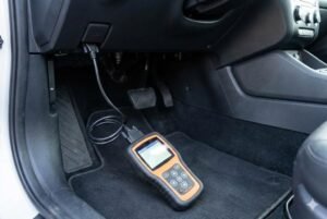 OBD scanner connected under car dashboard near the driver's seat for diagnostics.